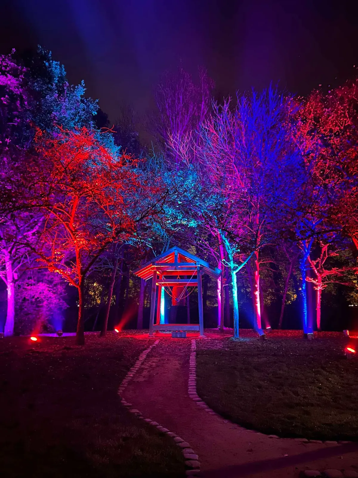 Pavillon de la cloche dans le jardin japonais entouré d’arbres éclairés en rouge, bleu et violet