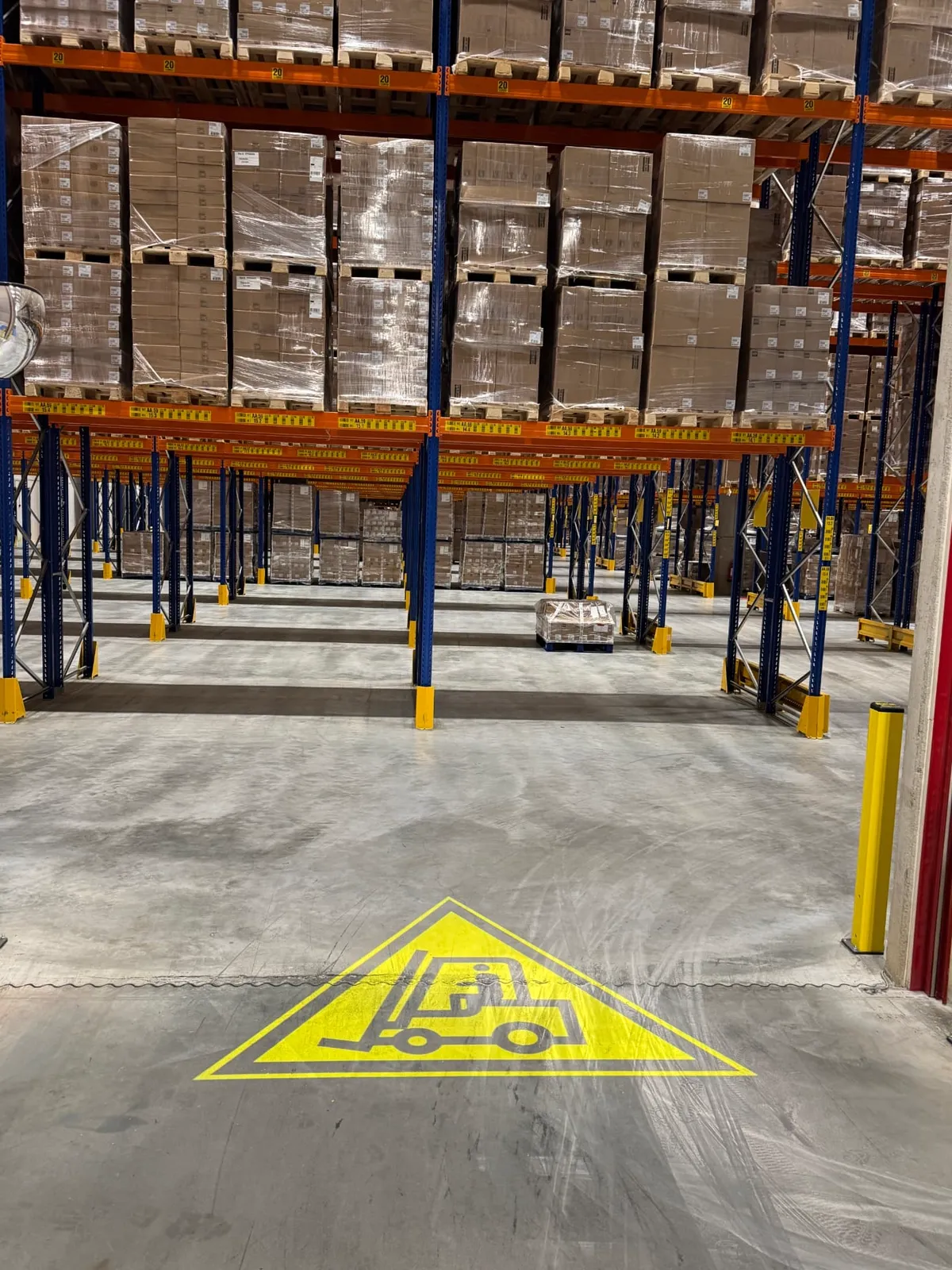 Yellow forklift warning sign projected onto the floor near the racking